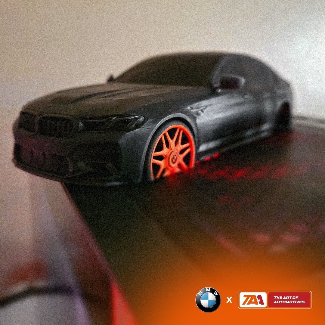 Black sports car model with orange wheels on display, BMW collaboration by The Art of Automotives