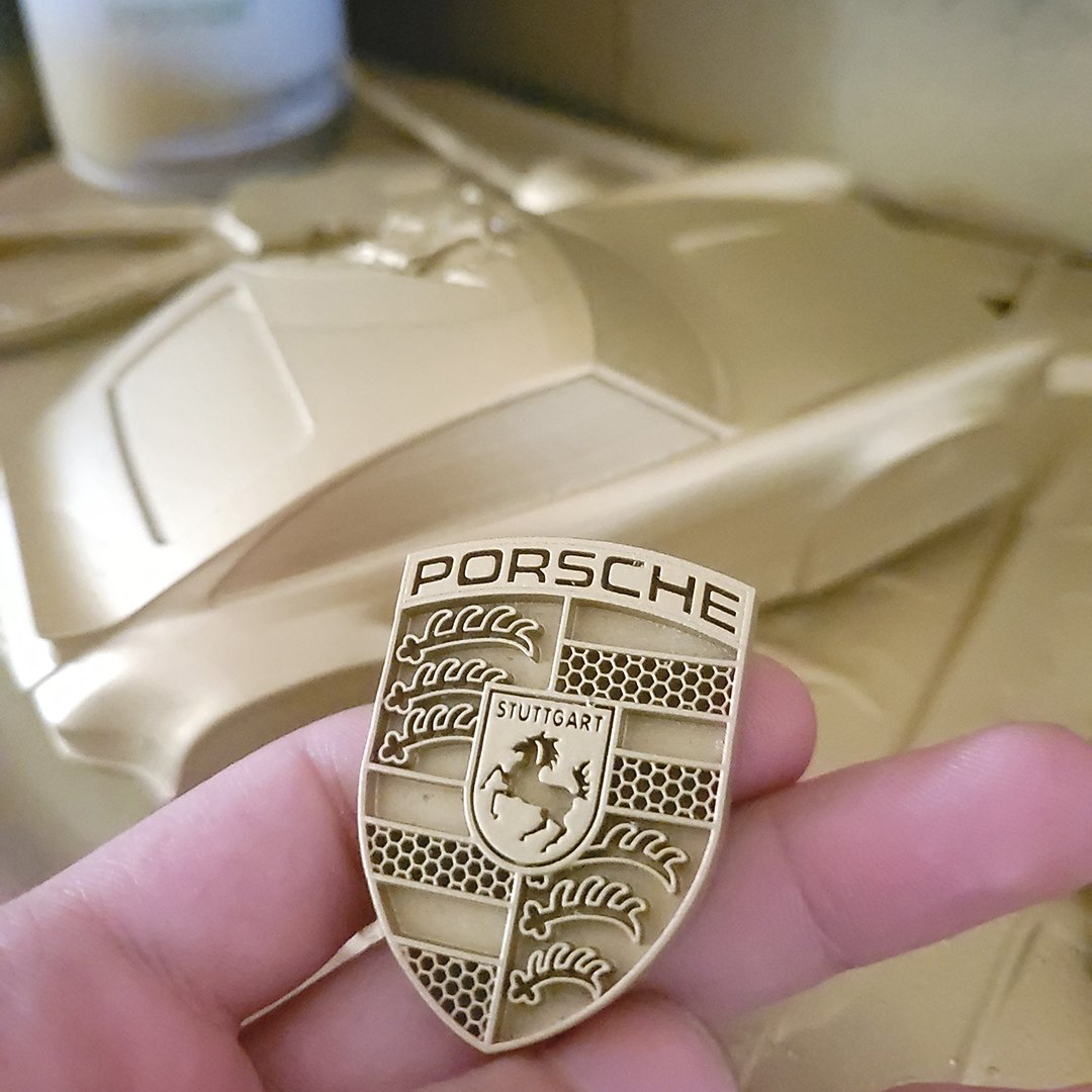Hand holding a freshly cast resin Porsche-style crest keychain prototype by the art of automotives