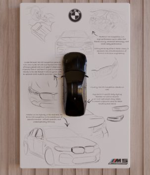 Top-view 3D-printed BMW M5 CS miniature in gloss-black finish mounted on a white panel with sketch background